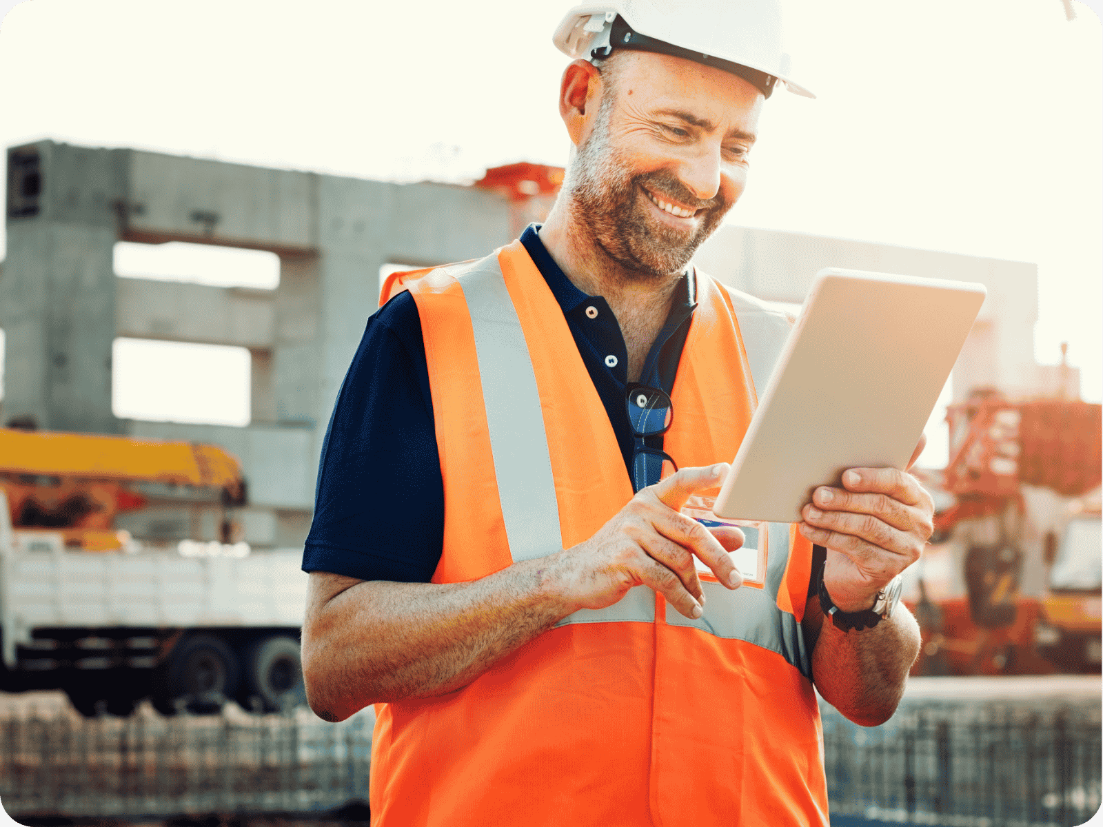 Field service technician in an orange safety vest and white hard hat reviewing job details on a tablet at a construction site.