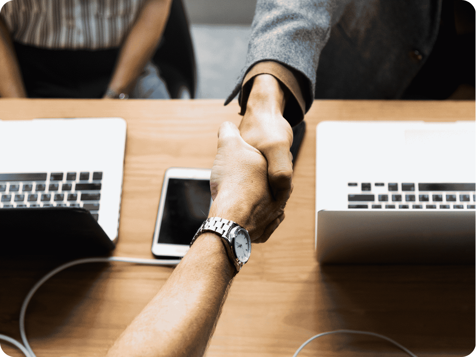 Two professionals shaking hands over laptops, symbolizing a software development partner for field service agreement