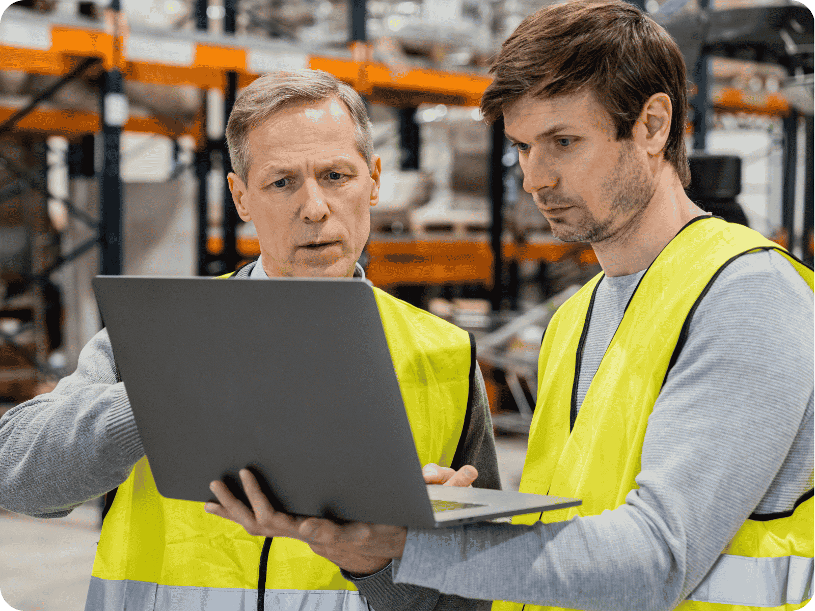 Two field service technicians in high-visibility vests reviewing predictive maintenance software on a laptop in a warehouse